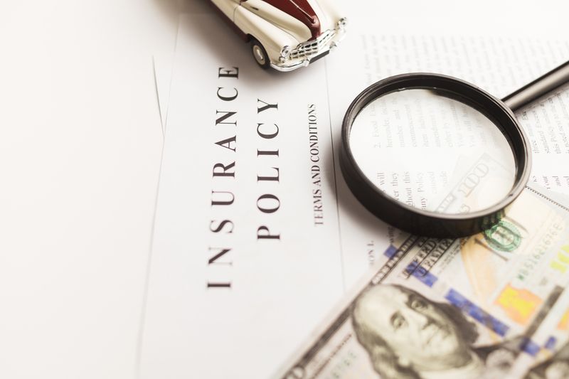An insurance policy under a magnifying glass, with a toy car and a dollar bill